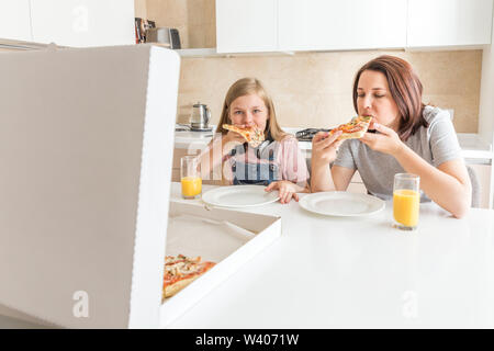 Mutter und Tochter in der Küche sitzen, essen Pizza und Spaß haben. Fokus auf Tochter Stockfoto