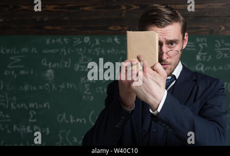 Sollten Sie es besser lernen. Lehrer formale Abnutzung und Gläser sieht Smart, schwarzes Brett Hintergrund. Mann unrasiert hält Buch vor. Lehrer insi Stockfoto