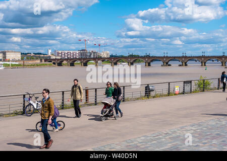 Bordeaux, Frankreich - 5. Mai 2019: Menschen gehen an der Promenade neben dem Fluss Garonne auf dem Hintergrund der Brücke Pont de Pierre in Bordeaux, Frankreich Stockfoto