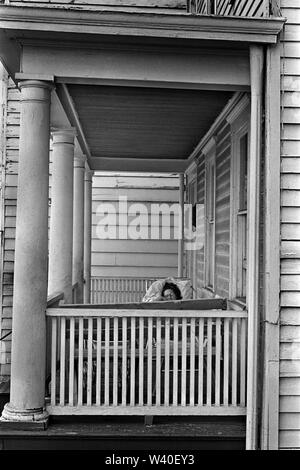 Altes, mit Holz verkleidetes Haus, weiß gestrichen, Holzverkleidung, Holzbretter, Äußere des Gebäudes. Eine Frau schläft auf ihrer Veranda. New Brunswick, New Jersey. 1969, USA 60S US HOMER SYKES Stockfoto