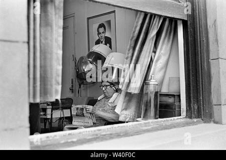 Frau, die Zeitung im Schönheitssalon liest, sitzt unter einem Haartrockner. Manhattan, New York. Gerahmtes Foto von Matinee Idol an der Wand hinter ihr. 1969, USA 60, US HOMER SYKES Stockfoto