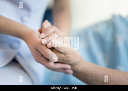 Krankenschwester sitzen auf einem Krankenhausbett neben eine ältere Frau helfende Hände, die Altenpflege Konzept Stockfoto