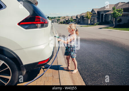 Vorschule wenig Kaukasische Mädchen waschen Auto in der Einfahrt vor dem Haus auf sonnigen Sommertag niedlich. Kids home Besorgungen Pflicht aufgaben verantwortung Konzept. Stockfoto