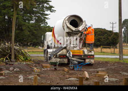 Annat, Canterbury, Neuseeland, 19. Juli 2019: Bauherren Schubkarre nassen Zement von betonmischer Lkw für Bohrpfähle auf einem ländlichen Gebäude sitzen Stockfoto