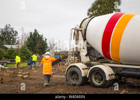 Annat, Canterbury, Neuseeland, 19. Juli 2019: Bauherren Schubkarre nassen Zement von betonmischer Lkw für Bohrpfähle auf einem ländlichen Gebäude sitzen Stockfoto