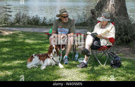 Im Schatten sitzen auf Camping Stühle, ein paar wahrscheinlich zurückgezogen, mit Ihrem Hund. Die Dame liest, der Gentleman hält die Spaniel an der Leine.. Stockfoto