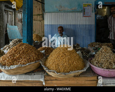 25 Jun 2019 Ladenbesitzer vor Körbe, mit unterschiedlichen Arten von getrockneten Fisch Shop am allgemeinen Markt Bezirk Raigadh Maharashtra Indien gefüttert Stockfoto