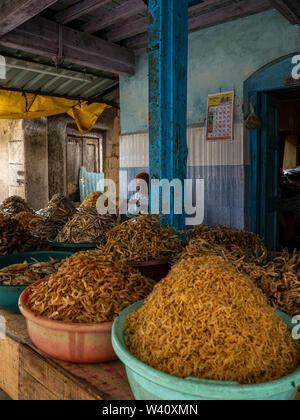 25 Jun 2019 Ladenbesitzer vor Körbe, mit unterschiedlichen Arten von getrockneten Fisch Shop am allgemeinen Markt Bezirk Raigadh Maharashtra Indien gefüttert Stockfoto