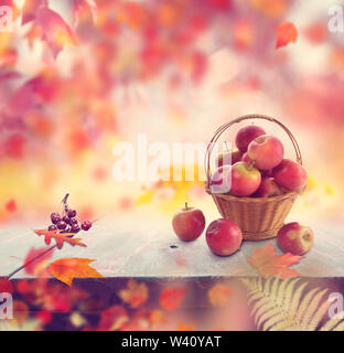 Rote Äpfel in einem Korb und Herbstlaub Hintergrund Stockfoto