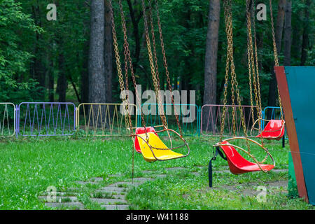 Mehrfarbig Gelb und Rot Kunststoff Sitze hängen die Ketten im Park für Unterhaltung und Spaß für Kinder und Erwachsene gegen die bac-Karussell Stockfoto