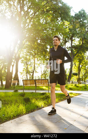 Portrait von gesunden athletischen Mann in Sportswear lächelnd und läuft, während Sie trainieren im sonnigen Green Park gekleidet Stockfoto