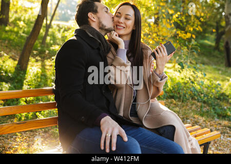 Fröhlicher junger paar Ausgaben Spaß Zeit im Park im Herbst, auf einer Bank sitzen, Musik hören mit Kopfhörern Stockfoto