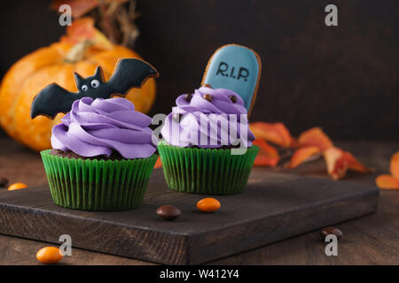 Festliche Halloween Cupcakes mit Lebkuchen Cookies - Tombstone und bat eingerichtet. Der dunkle Hintergrund mit Kürbis und kopieren Sie Raum, selektive konzentrieren. Stockfoto