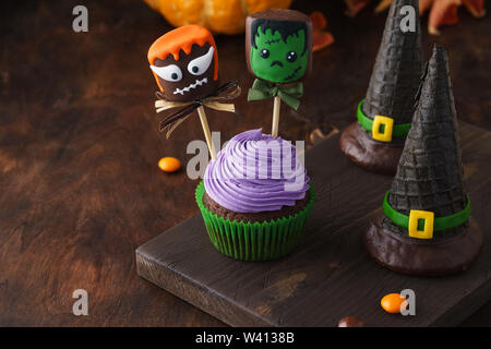 Festliche Halloween Kuchen dekoriert mit Kuchen oder Schokolade getauchte Marshmallow Monster mit lustigen Gesichtern und Wafer Hexe Hüte. Der dunkle Hintergrund mit Stockfoto