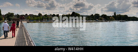 Altnau, TG/Schweiz - 14. Juli 2019: Touristen zu Fuß entlang der langen Pier in Altnau mit Panorama Blick auf das Ufer des Bodensees. Stockfoto