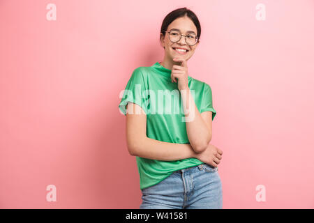 Foto von Brünette junge Mädchen tragen runde Brille berühren Ihr Kinn und lächelnd an der Kamera über rosa Hintergrund isoliert Stockfoto