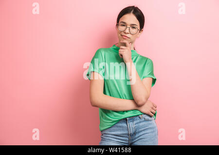 Foto der sympathische junge Mädchen tragen runde Brille berühren Ihr Kinn und lächelnd an der Kamera über rosa Hintergrund isoliert Stockfoto