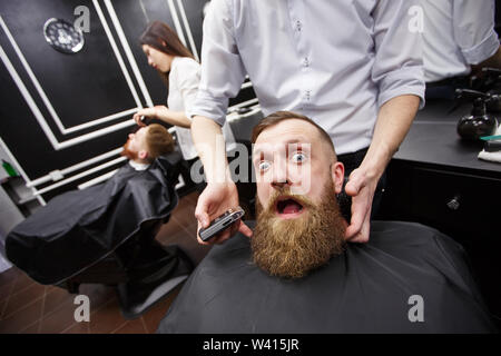 Bärtiger Mann mit Angst sitzt in einem Barbershop Stockfoto