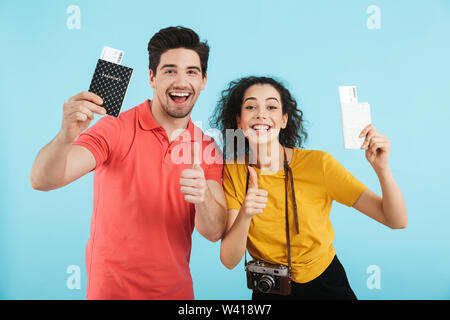 Fröhlicher junger Paare, die auf blauen Hintergrund isoliert, Pässe und Flugtickets Stockfoto