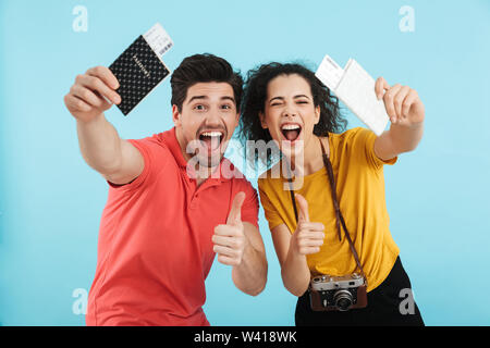 Fröhlicher junger Paare, die auf blauen Hintergrund isoliert, Pässe und Flugtickets Stockfoto