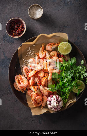 Rohe Garnelen in einer Pfanne Kochen mit Zutaten für die Zubereitung gebratene Garnelen auf einem dunklen Hintergrund der Ansicht von oben Stockfoto