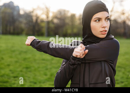 Portrait von Fitness muslimische Frau in religiösen Schwarz hijab ihre Arme ausdehnen, während Sie trainieren im Green Park im Freien gekleidet Stockfoto