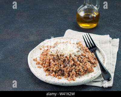 Buchweizen Risotto mit getrockneten Pilzen in Handwerk Platte auf schwarzem Zement Hintergrund. Glutenfreie und vegetarische Buchweizen Rezept Ideen. Platz kopieren Stockfoto