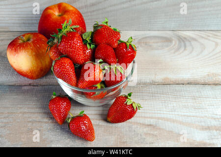 Äpfel, Erdbeeren liegen in einem kleinen Teller auf einem natürlichen Holzhintergrund. Foto von oben Stockfoto