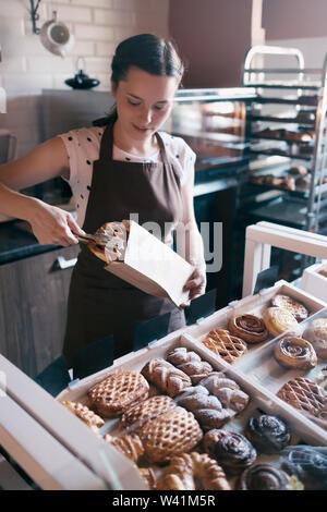 Ziemlich lächelnd weibliche Arbeitnehmer Auswahl Muffins aus einem Zähler Anzeige im kleinen Bäckerei an einen Kunden verkaufen, Family Business Konzept Stockfoto