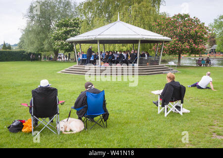 Das Sitzen im Park an der Mühle Wiesen, Henley-on-Thames, hören auf die Brass Band spielen auf der Bühne Stockfoto