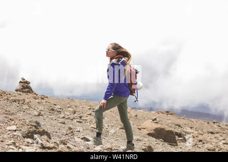 Formschöne Blondine mit einem Rest zwischen langen Entfernungen und Klettern auf den Berg. Hohe Kilimanjaro top mit Felsen und keine Pflanzen. Weiße Wolken hinter Stockfoto