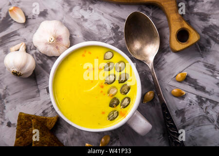 Warme würzige Kürbissuppe mit Knoblauch garniert mit Kürbiskernen in einem großen weißen Schale auf einem grauen Tabelle. Herbst traditionelles Gericht. Ansicht von oben, flach Stockfoto