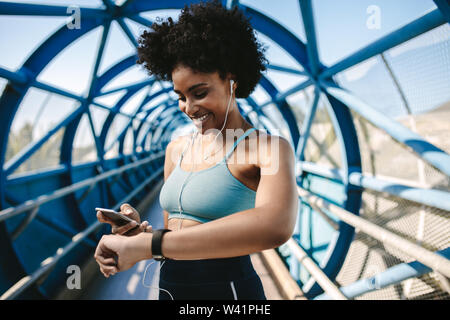 Passen Läuferin mit smart Watch und Handy ihre Leistung zu überwachen. Sportlerin Gefühl glücklich nach dem Workout. Stockfoto