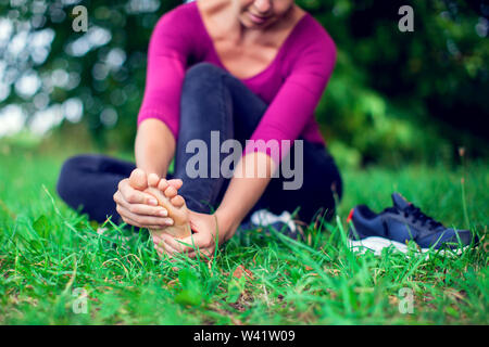 Fußschmerz. Frau sitzt auf Gras. Ihre Hand am Fuß erwischt. In schmerzende Füße und Stretching Muskeln Ermüdung Schmerzen zu lindern. Gesundheit Konzept. Stockfoto