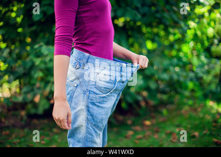 Junge Frau mit großen Losen Jeans mit Apfel in der Hand Outdoor - Gewicht-Verlust-Konzept Stockfoto