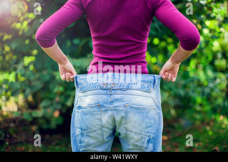 Junge Frau mit großen Losen Jeans mit Apfel in der Hand Outdoor - Gewicht-Verlust-Konzept Stockfoto