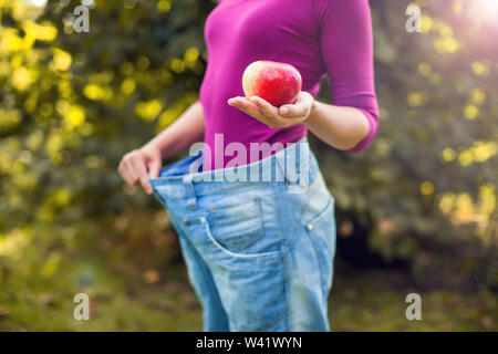 Junge Frau mit großen Losen Jeans mit Apfel in der Hand Outdoor - Gewicht-Verlust-Konzept Stockfoto