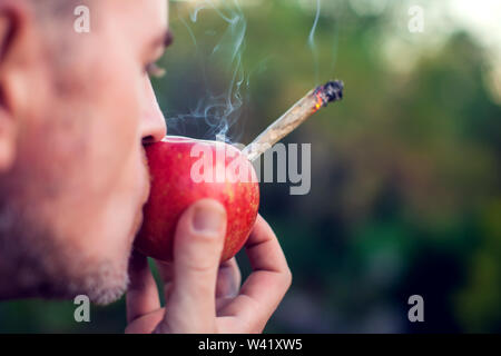 Ein Mann das Rauchen von Marihuana gemeinsame durch einen Apfel. Leichte Drogen Konzept Stockfoto