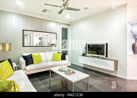 Designer Wohnraum mit Sofa, einem Tisch, einem Ventilator, Deckenleuchten, und einem an der Wand montierten Fernseher Stockfoto