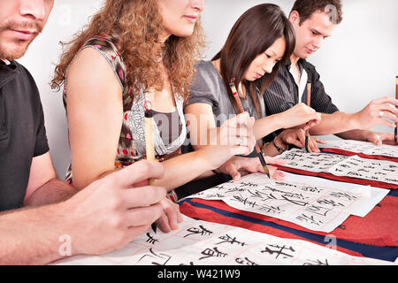 Gruppe von Studenten mit dem Schreiben von Buchstaben wie Chinesisch oder Japanisch auf Papier, mit Pinsel auf dem Papier vertikal Stockfoto