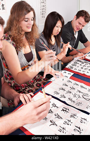 Die Schüler sprechen und schreiben Buchstaben auf weißem Papiere mit Bürsten Stockfoto