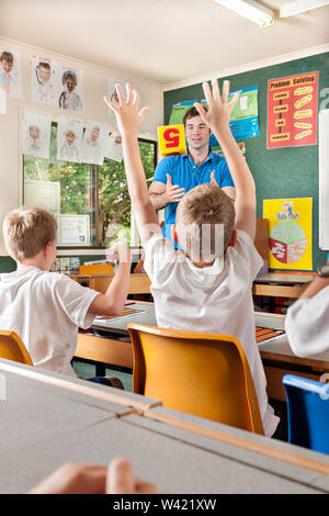 Lehrer lehrt Kinder im Klassenzimmer mit einem Würfel und Fragen, ein Kind die Hände hoch Stockfoto