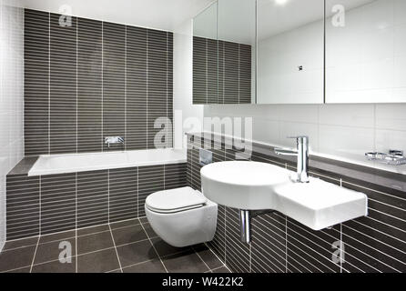 Ein minimalistisches Badezimmer verfügt über eine Badewanne, ein Waschbecken, einen an der Wand WC-Sitz und Spiegel Stockfoto
