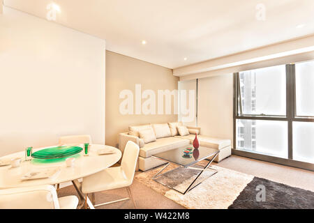 City Apartment mit modernen Look und Tabellen, Blick auf die Stadt kann durch die Fenster sehen, classic Kissen auf dem Sofa, bunten Teppich einschließlich Designs atta Stockfoto