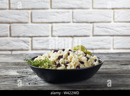 Karibik, Reis und rote Bohnen gekocht mit Kokosmilch, gewürzt mit Knoblauch, Zwiebeln und kreolischen Spice in einem schwarzen Schüssel mit einer Mauer an der backgroun Stockfoto