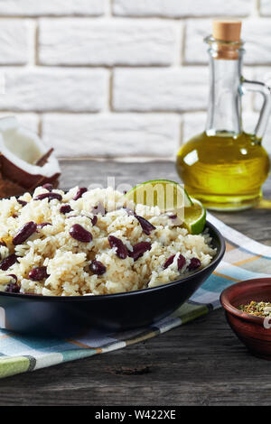 Karibik, Reis und rote Bohnen mit Kokosmilch, gewürzt mit Knoblauch, Zwiebeln und kreolischen Gewürzen in eine Schüssel mit Zutaten und ein Glas Wasser wi gekocht Stockfoto