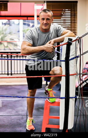 Junger Mann wartet im Boxen, Innenraum eines luxuriösen Fitnessraum, schwere Übung Werkzeuge in der Nähe von Mauer, er sieht aus wie Body Builder, Schuhe bunt sind. Stockfoto