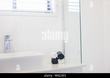 Blick auf ein Waschbecken und einen Wasserhahn mit vier zusammengerollt Handtücher in Schwarz und Weiß auf der Seite Tresen Stockfoto