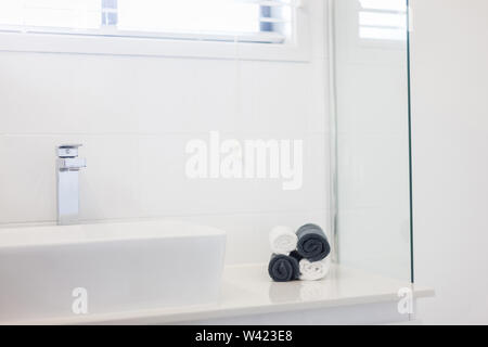 Blick auf ein Waschbecken und einen Wasserhahn mit vier zusammengerollt Handtücher in Schwarz und Weiß auf der Seite Tresen Stockfoto