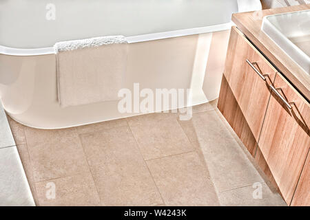 Watertub schließen oben mit einem Fliesenboden im Badezimmer mit weisser Wolle Handtuch hängen an der Badewanne neben dem Holz- cupboar Stockfoto